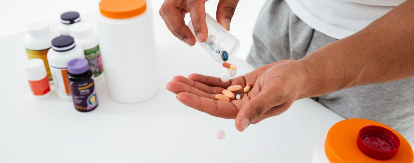 Cropped image of young sportsman standing over white background holding vitamins and sport pills.